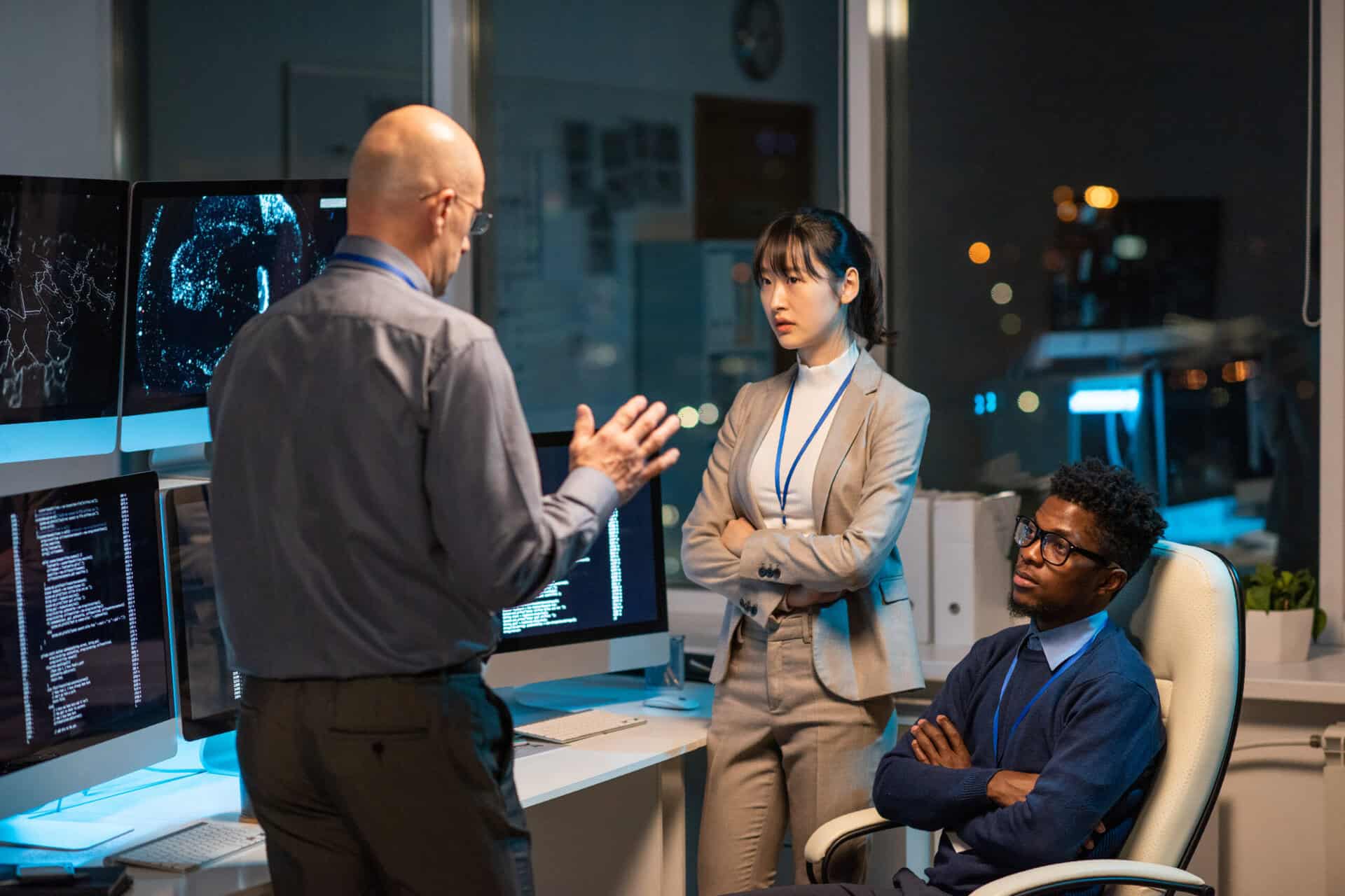 Mature manager giving instructions to young intercultural subordinates at working meeting late at night